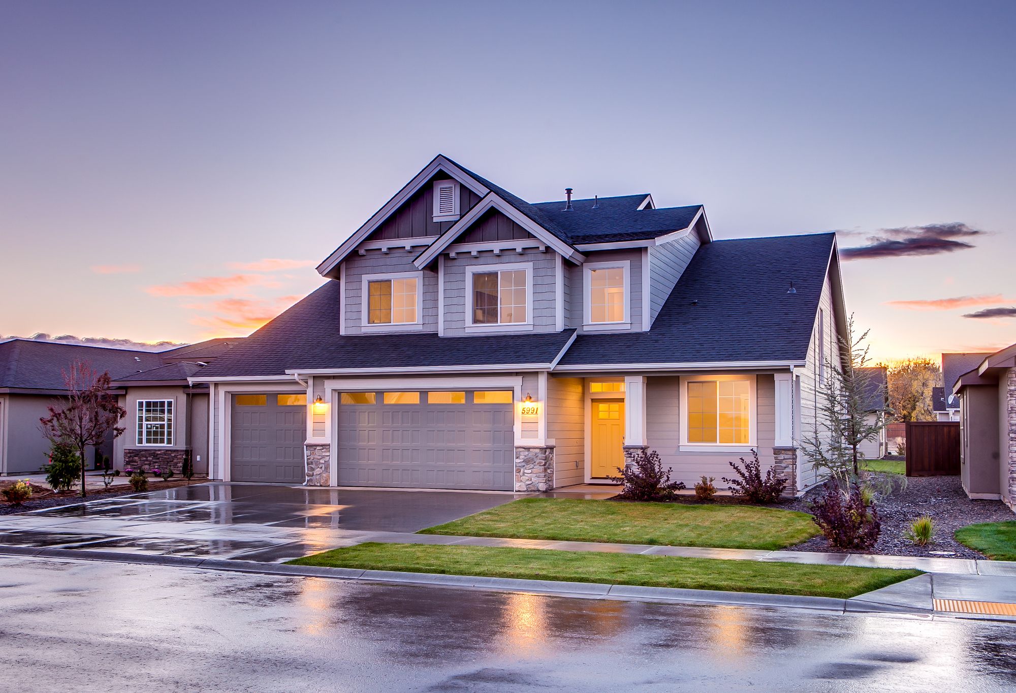 A family home at dusk with warm light glowing from the windows and the front door