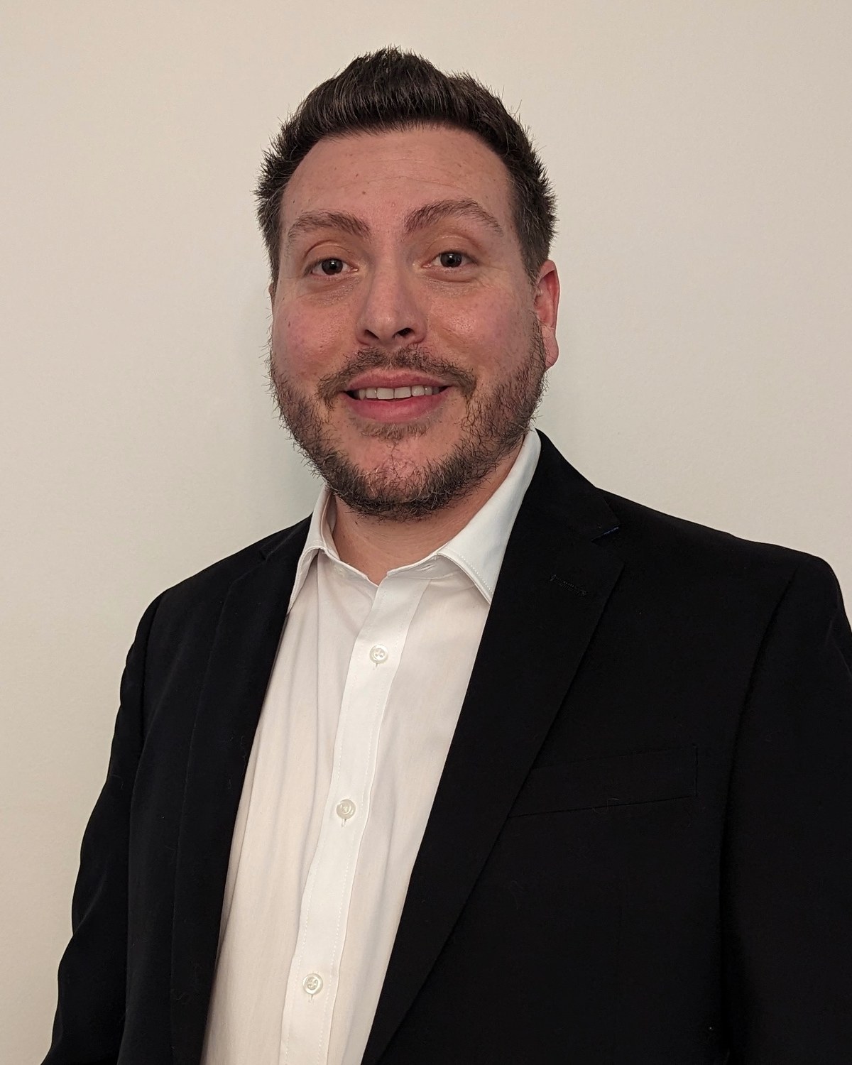 Jessy Casaus Sr. in a black suit jacket and open white shirt, smiling